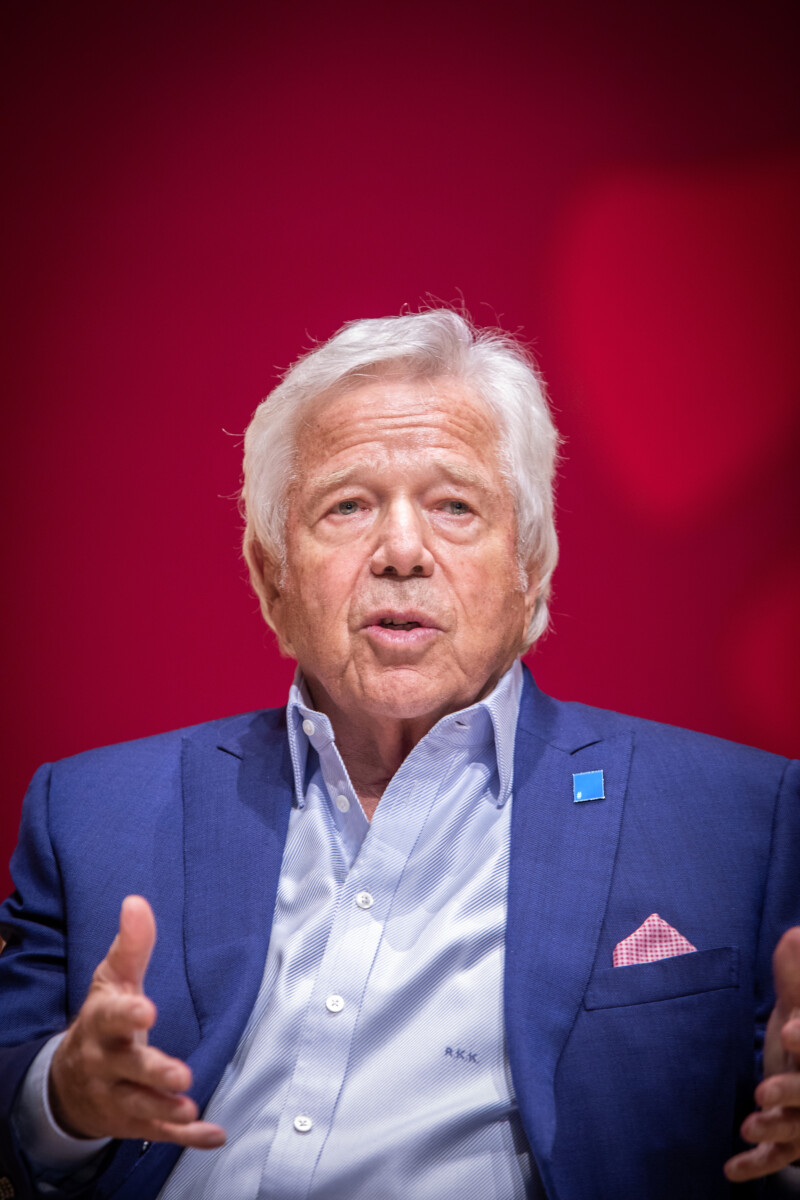 Robert Kraft, the founder of the Foundation to Combat Antisemitism, is in conversation. He is set against a red background. On his jacket lapel is a Blue Square pin.