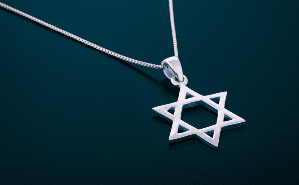 A silver Star of David on a silver pendant set against a teal background.