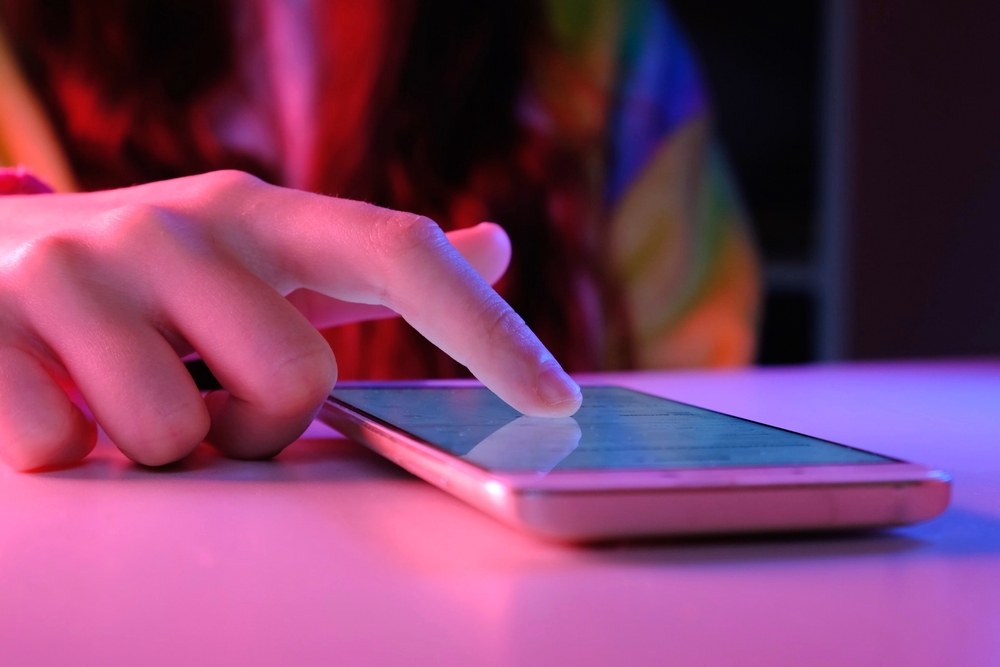 A cell phone on a table with someone tapping on it set against bright, vivid lights.